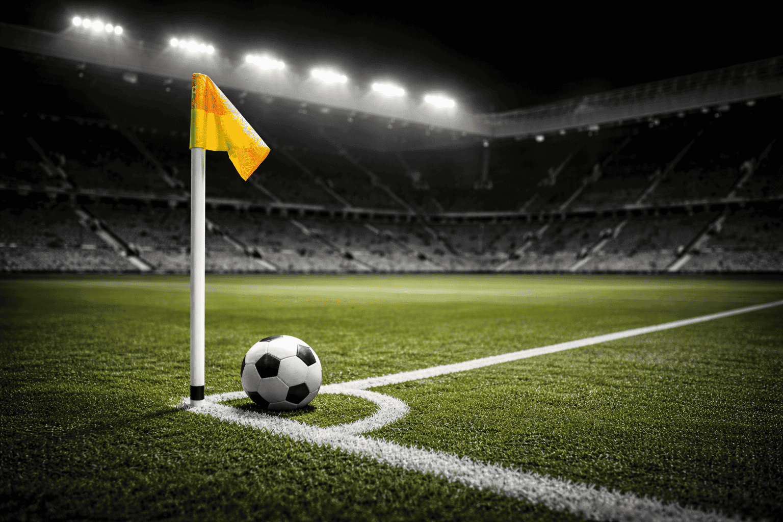 Night stadium corner with a football resting beside a brightly coloured corner flag on vivid green grass